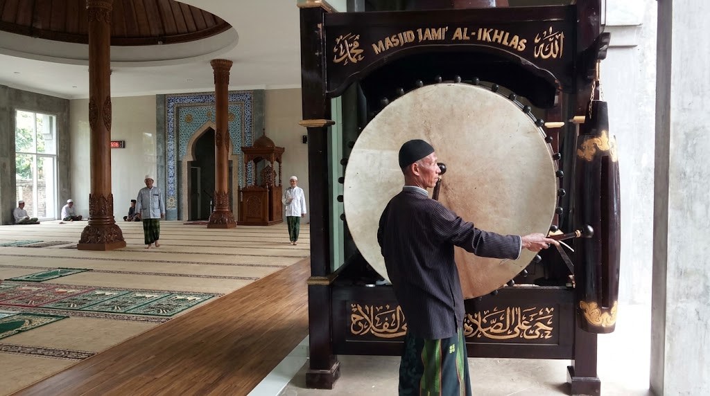 Seorang pria menabuh bedug besar berkaligrafi di dalam masjid